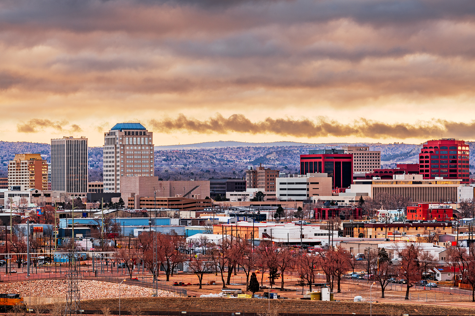 colorado-springs-colorado-usa-downtown-city-skyline Downtown Colorado Springs skyline at sunset, featuring office buildings, mountains in the background, and dramatic clouds overhead.